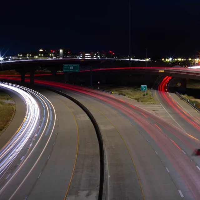 Long-exposure light trails from traffic curving through a road junction at
                  night.