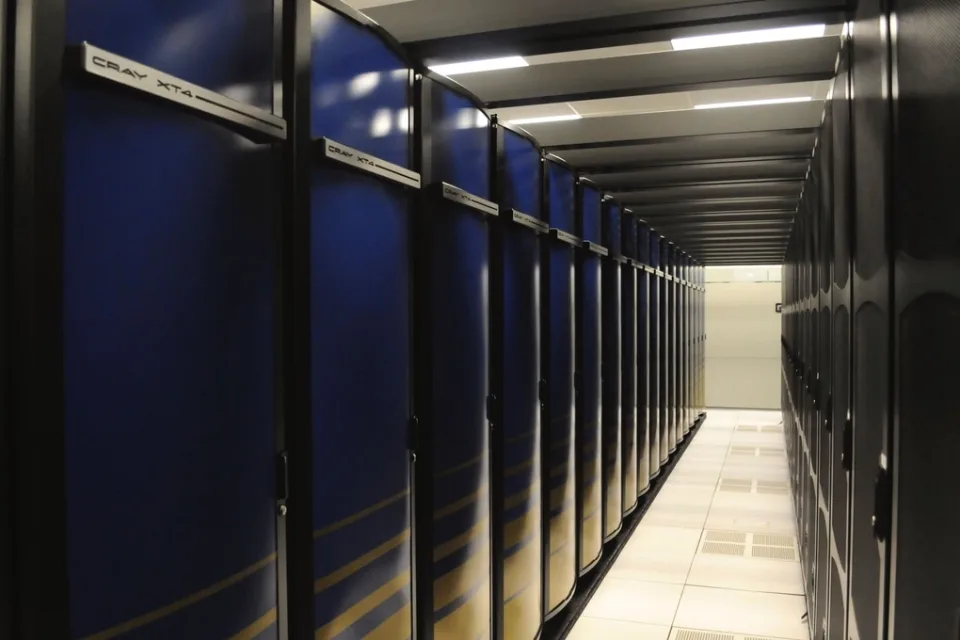 A row of supercomputer cabinets in a machine hall, lit from within.