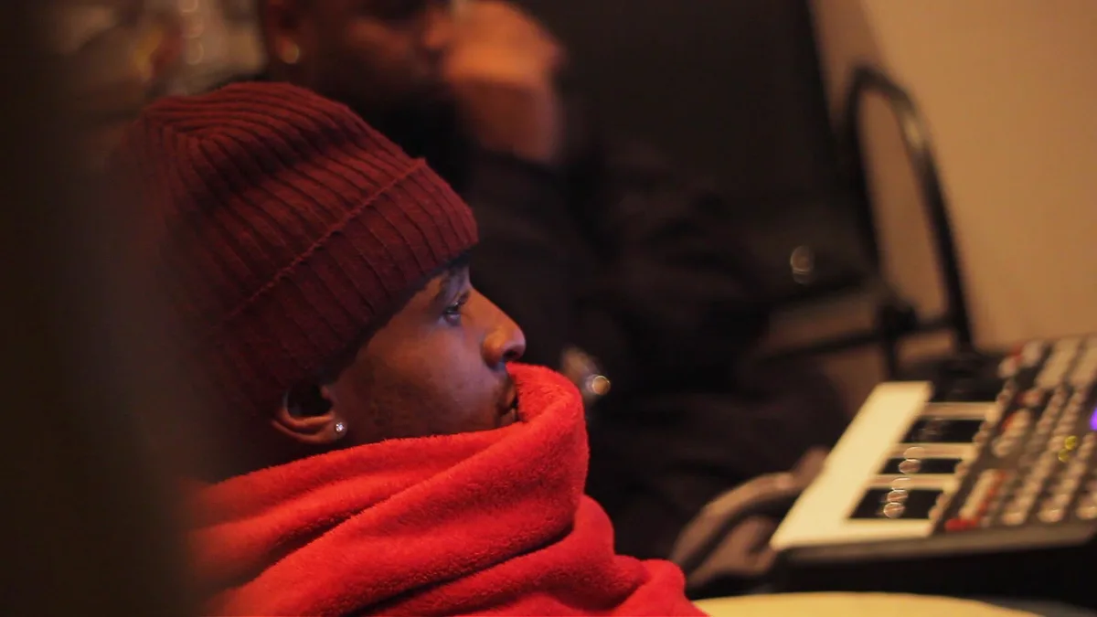 A musician in a red beanie and scarf leaning over a sampler in low light.
