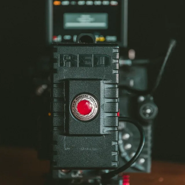 A cine camera on a dark ground, lens forward, its body worn from use.