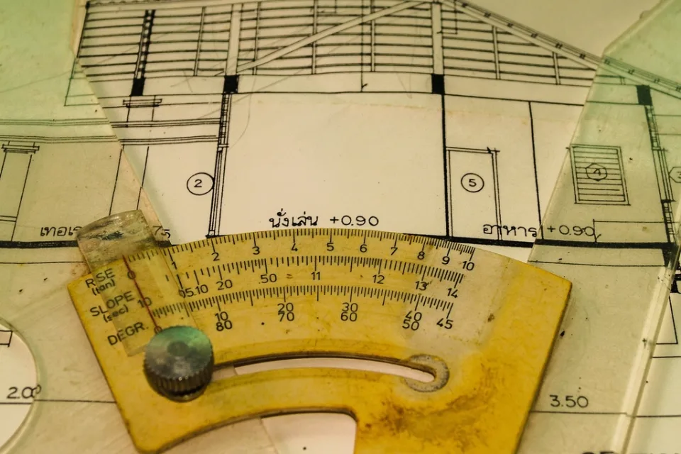 Architectural drawings on a desk with a worn yellow scale rule laid
                  across them.