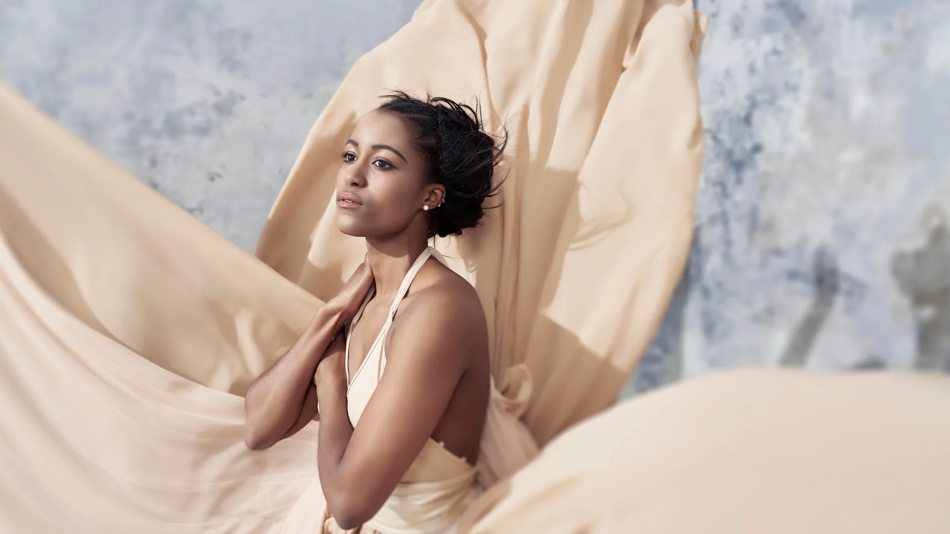 A woman posed among flowing cream fabric.