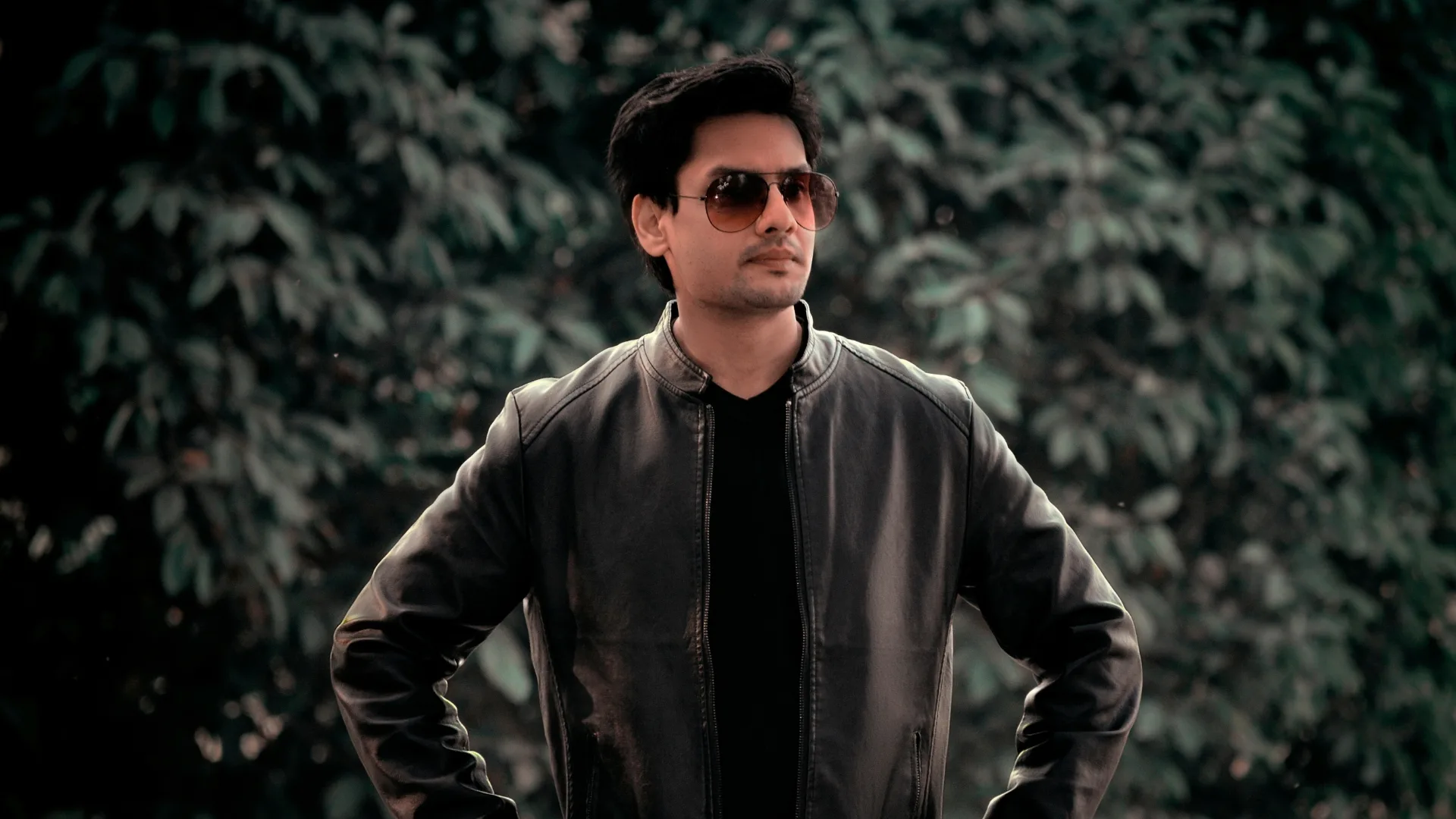 A man in sunglasses and a black jacket standing outdoors.