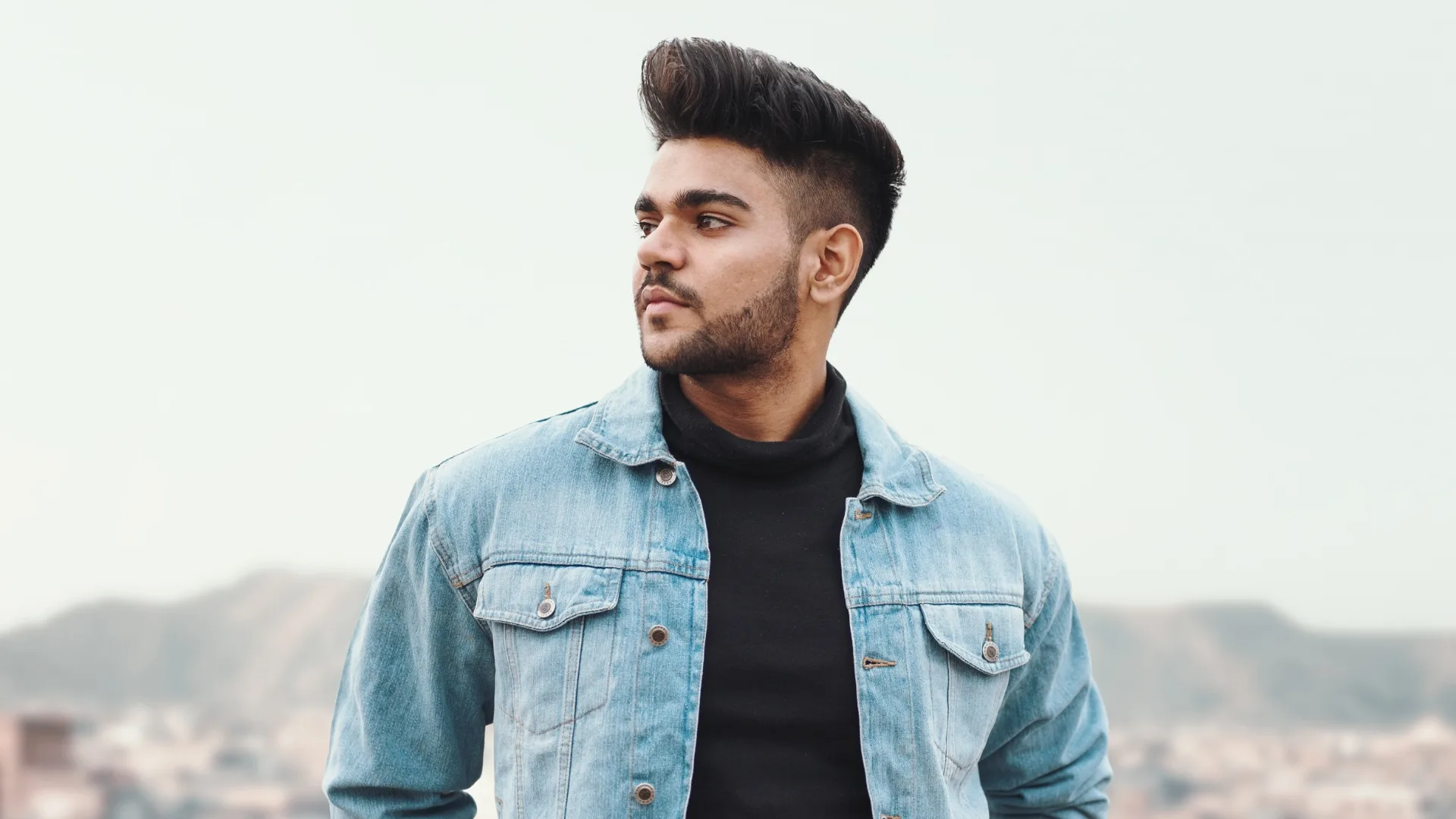A man in a denim jacket posed against a pale landscape.