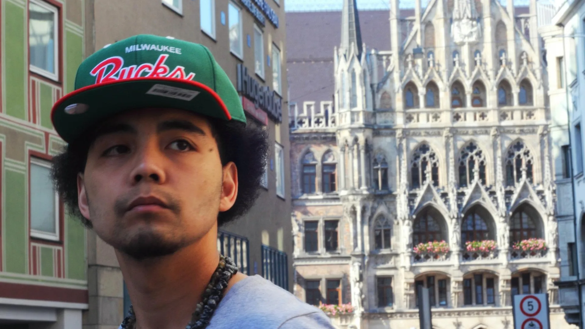 A street portrait of a man in a baseball cap with ornate architecture behind him.
